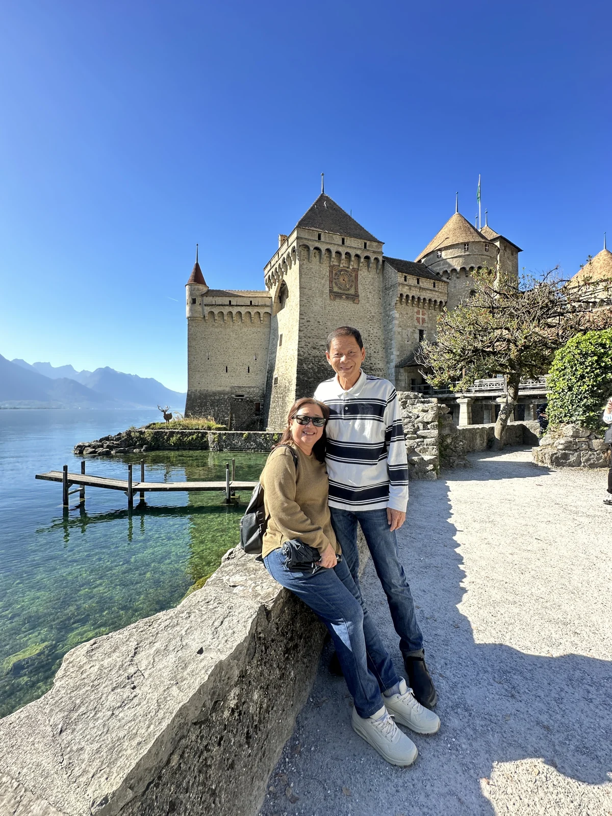 Travellers posing by a lakeside castle in Switzerland